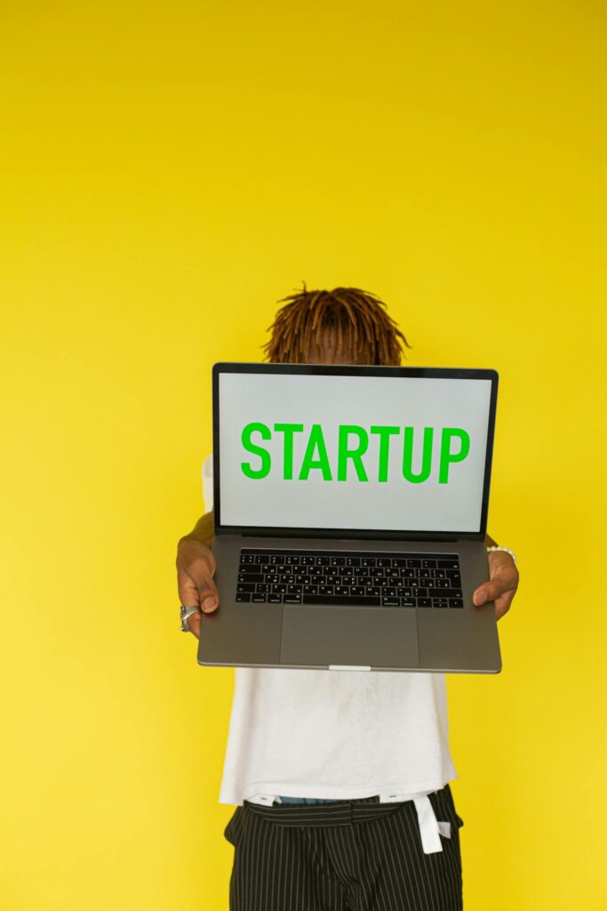 Person holding a laptop with 'STARTUP' text against a bright yellow background, symbolizing innovation.